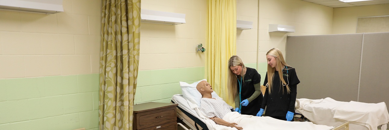 Two cna students work with a mannequin